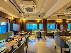 A restaurant with booths and tables, wooden paneling, and large windows. - Zip By Spree Hotels Shirdi (Rahata)