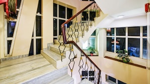 A multi-level interior with a marble staircase, a geometric metal railing, and large windows. - Hotel Batra Holiday Home (New Delhi)