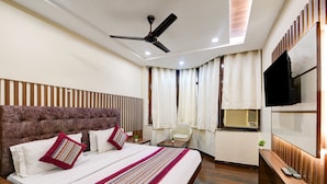 A modern hotel room with a large bed, a ceiling fan, a TV, and a window with curtains. - Hotel Batra Holiday Home (New Delhi)