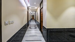 A long, narrow hallway with a marble floor, wooden doors, and recessed lighting. - Hotel Batra Holiday Home (New Delhi)