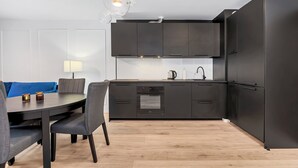 A modern kitchen with dark cabinetry, a built-in oven, and a dining area with a table and chairs.