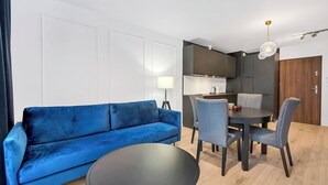 A modern living room with a blue sofa, a round coffee table, and a dining area with chairs and a table.