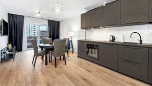 A modern kitchen with dark cabinets, a built-in oven, and a dining area with a round table and chairs.