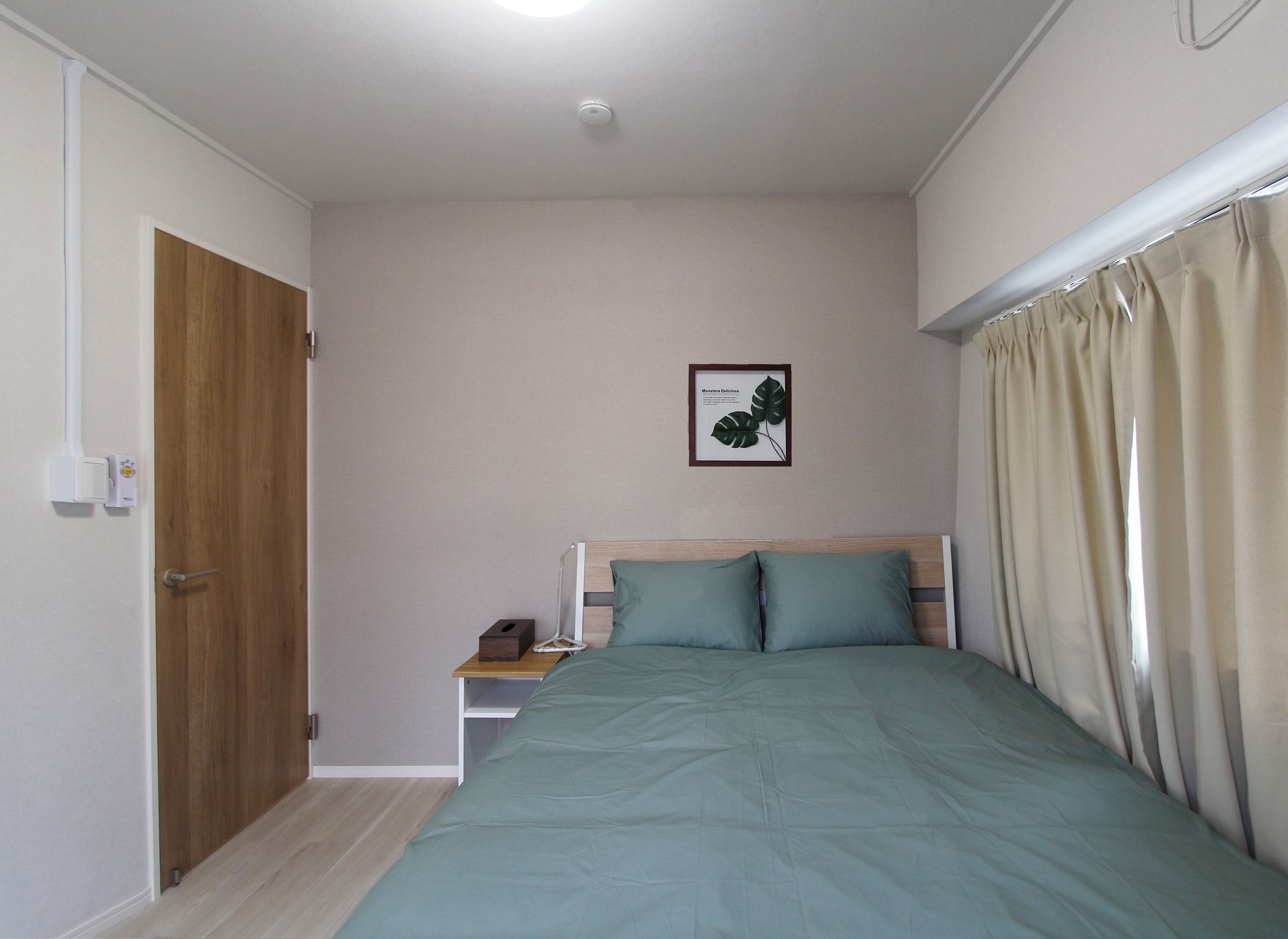 A bedroom with a bed, a nightstand, a wooden door, and a wall-mounted light fixture.