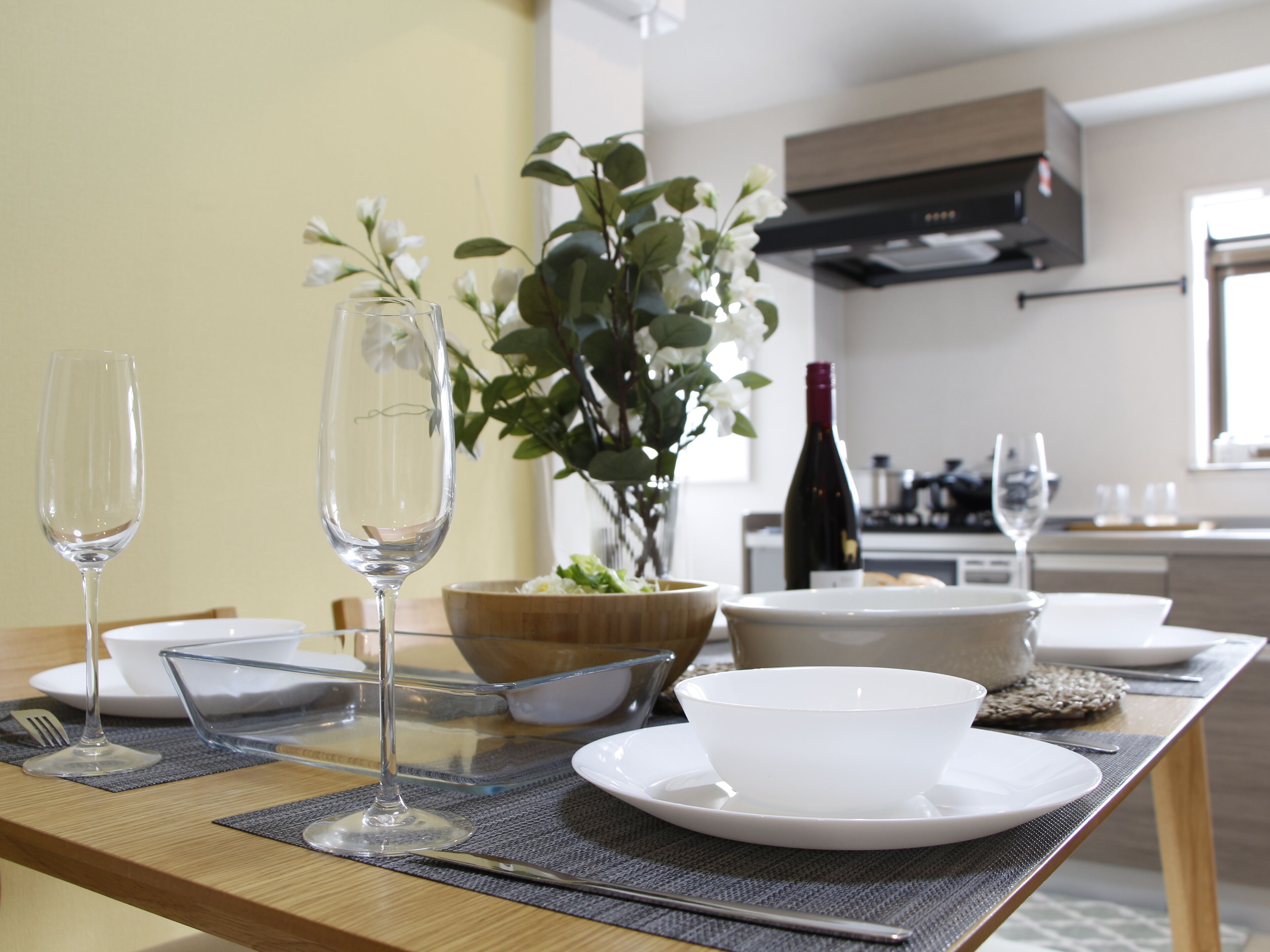 A dining table with a clear glass wine glass, a white bowl, and a wooden bowl.