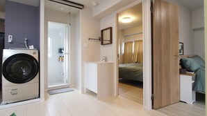 Une pièce compacte et bien éclairée, équipée d’un lave-linge, d’une petite salle de bain et d’un lit.