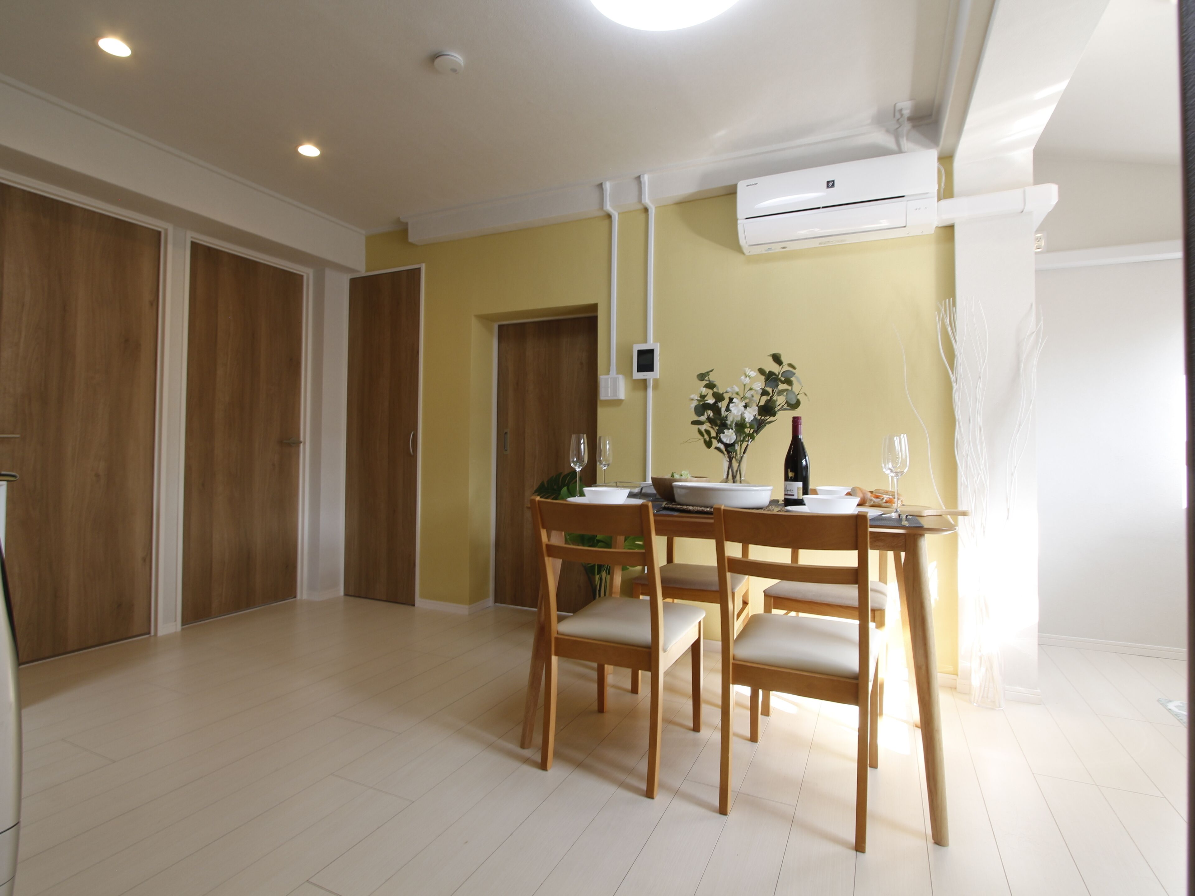 A dining area with a table set for four, wooden chairs, a vase with flowers, and a bottle of wine.