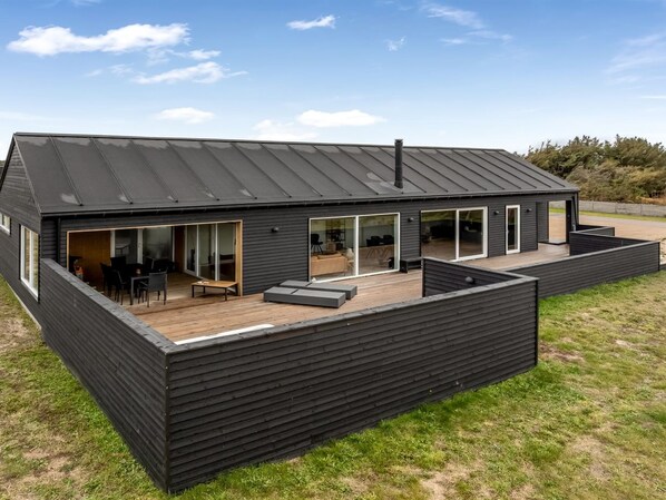 A modern black house with a large deck, sliding glass doors, and a sloped roof.