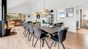 A spacious dining area with a long table, black chairs, and pendant lights.
