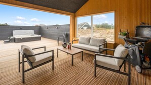 A spacious outdoor area with a wooden deck, a hot tub, a sofa, and a grill.