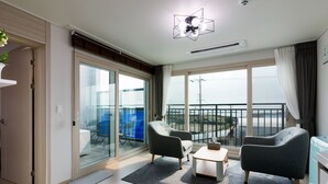 Una sala de estar moderna con un amplio ventanal corredera que da a un balcón, un ventilador de techo y vistas al exterior.