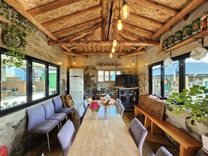 Ein rustikales Interieur mit freiliegenden Holzbalken, einem langen Esstisch aus Holz und gemütlicher Sitzgelegenheit.