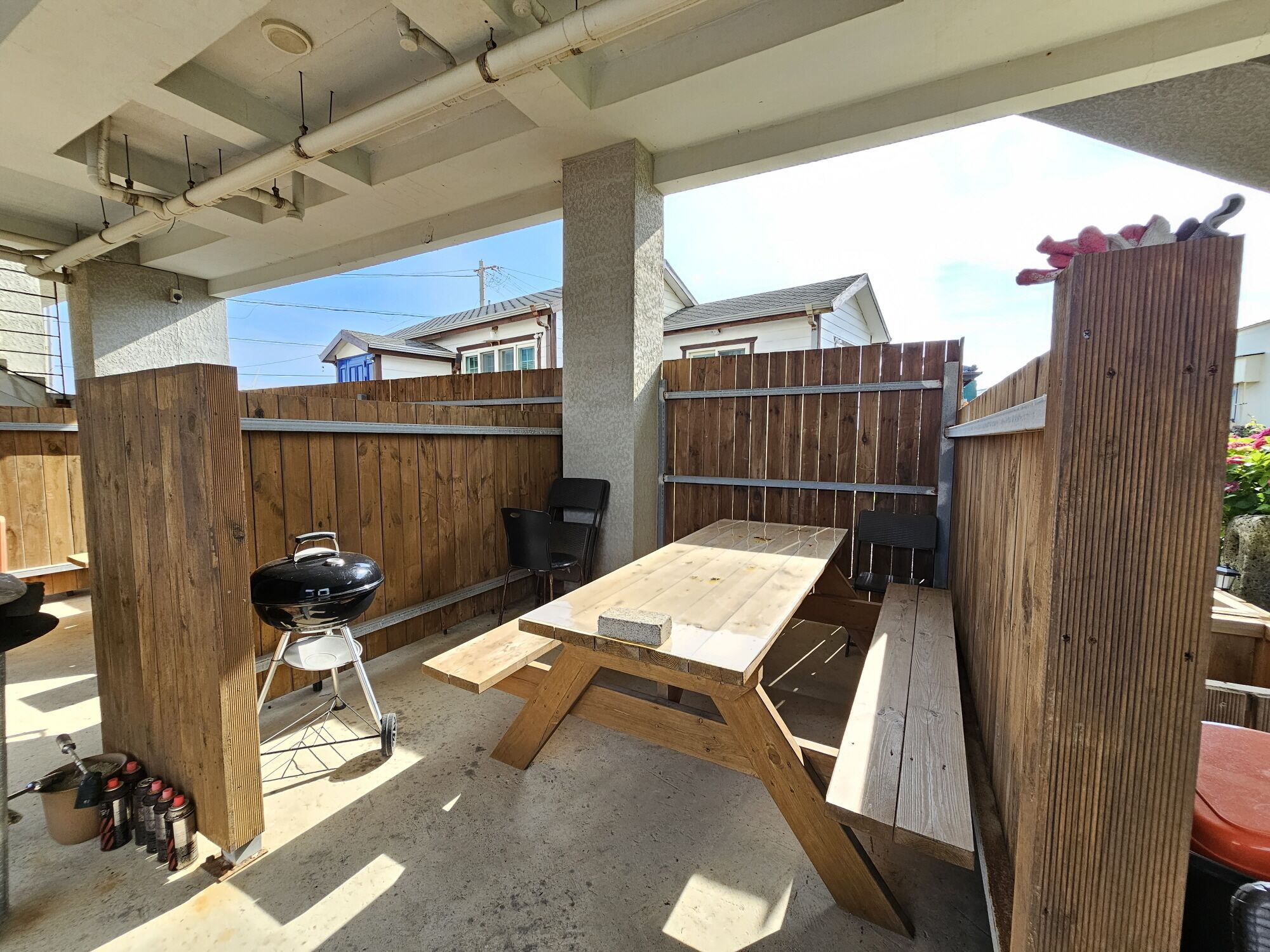 An outdoor patio with a wooden table and chairs, a barbecue grill, and a wooden fence.