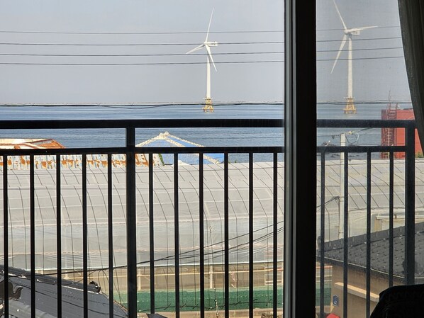 Blick auf Windkraftanlagen über einem Gewässer, im Vordergrund ein Metallzaun.