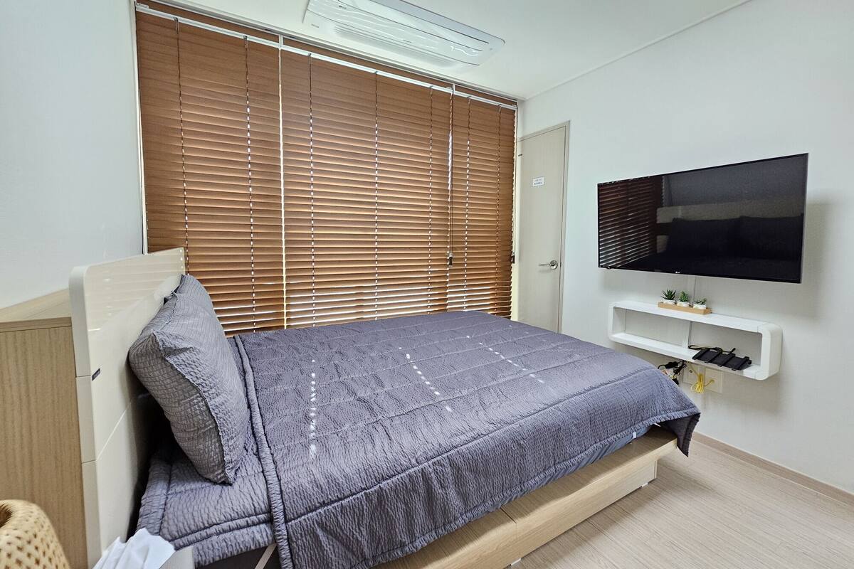 Een slaapkamer met een bed, een aan de muur bevestigde televisie en een raam met zonwering.