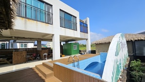 Un edificio moderno con piscina, terraza de madera y una estructura de techo de paja.