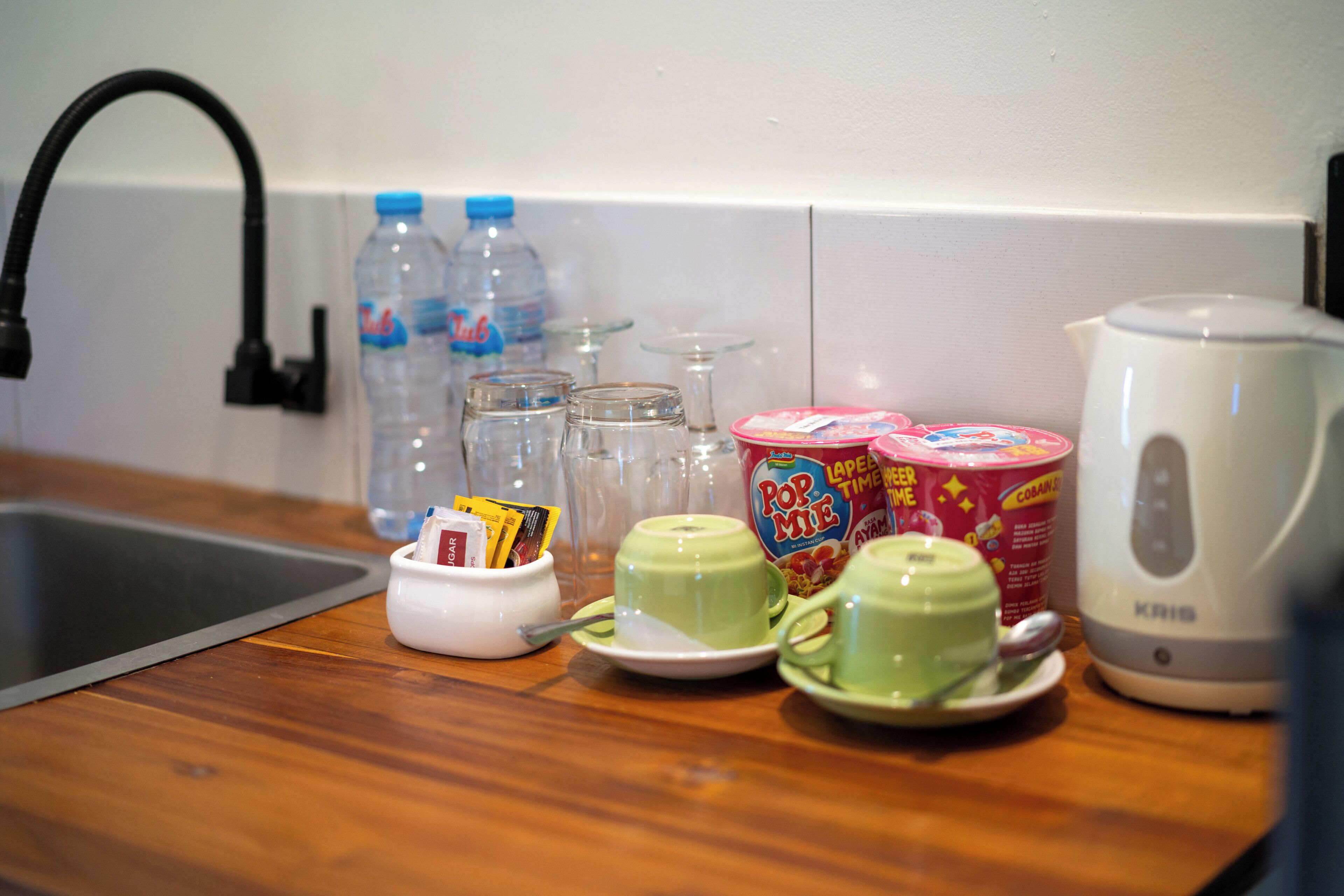 A kitchen counter with a kettle, cups, jars, and a water bottle.