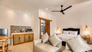 A modern hotel room with a bed, two sofas, a dining area with a table and chairs, a kitchen, and a ceiling fan. - Lala Panzi Villa (Jimbaran)