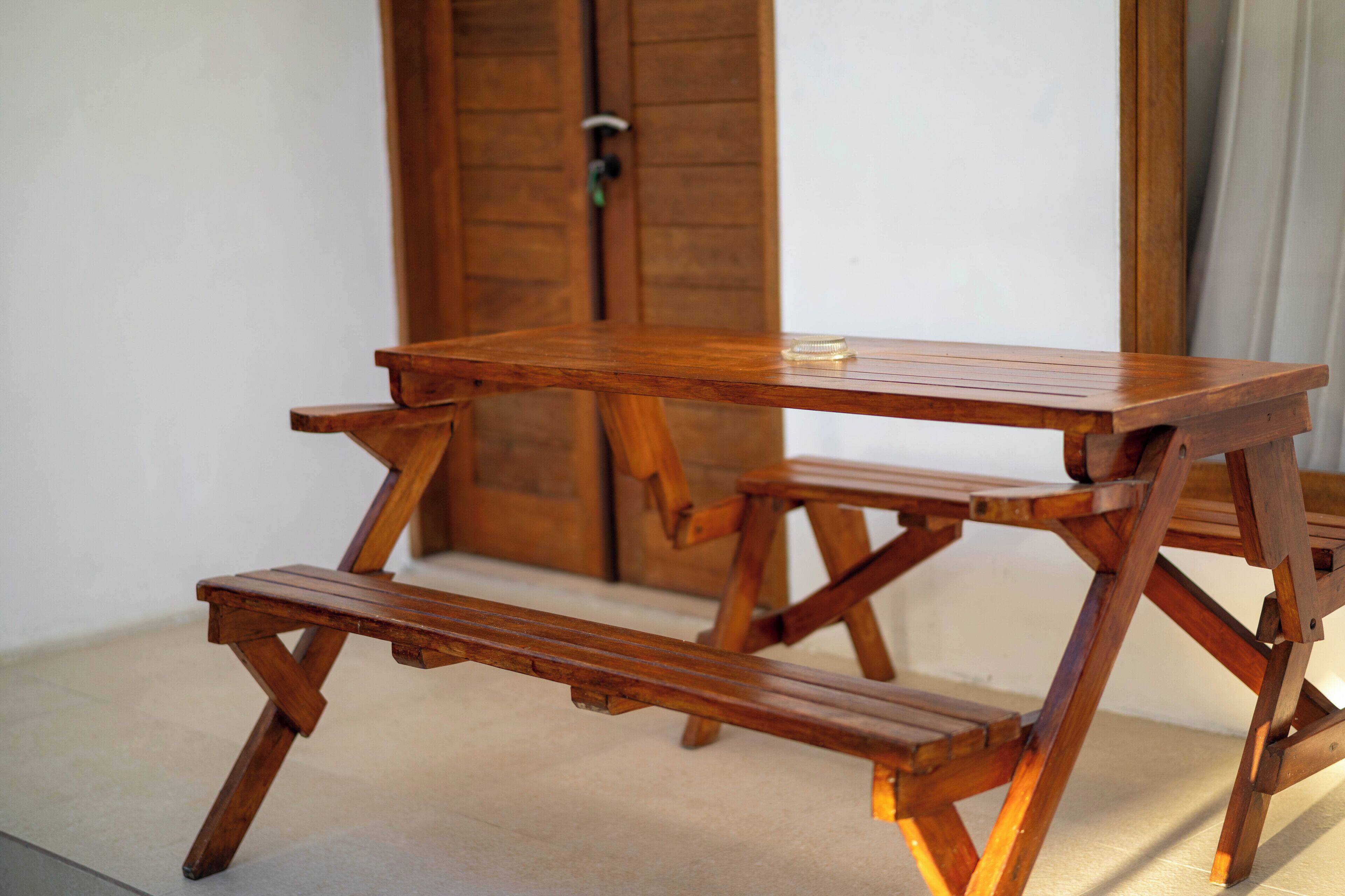 A wooden picnic table with benches, positioned in front of a wooden door.