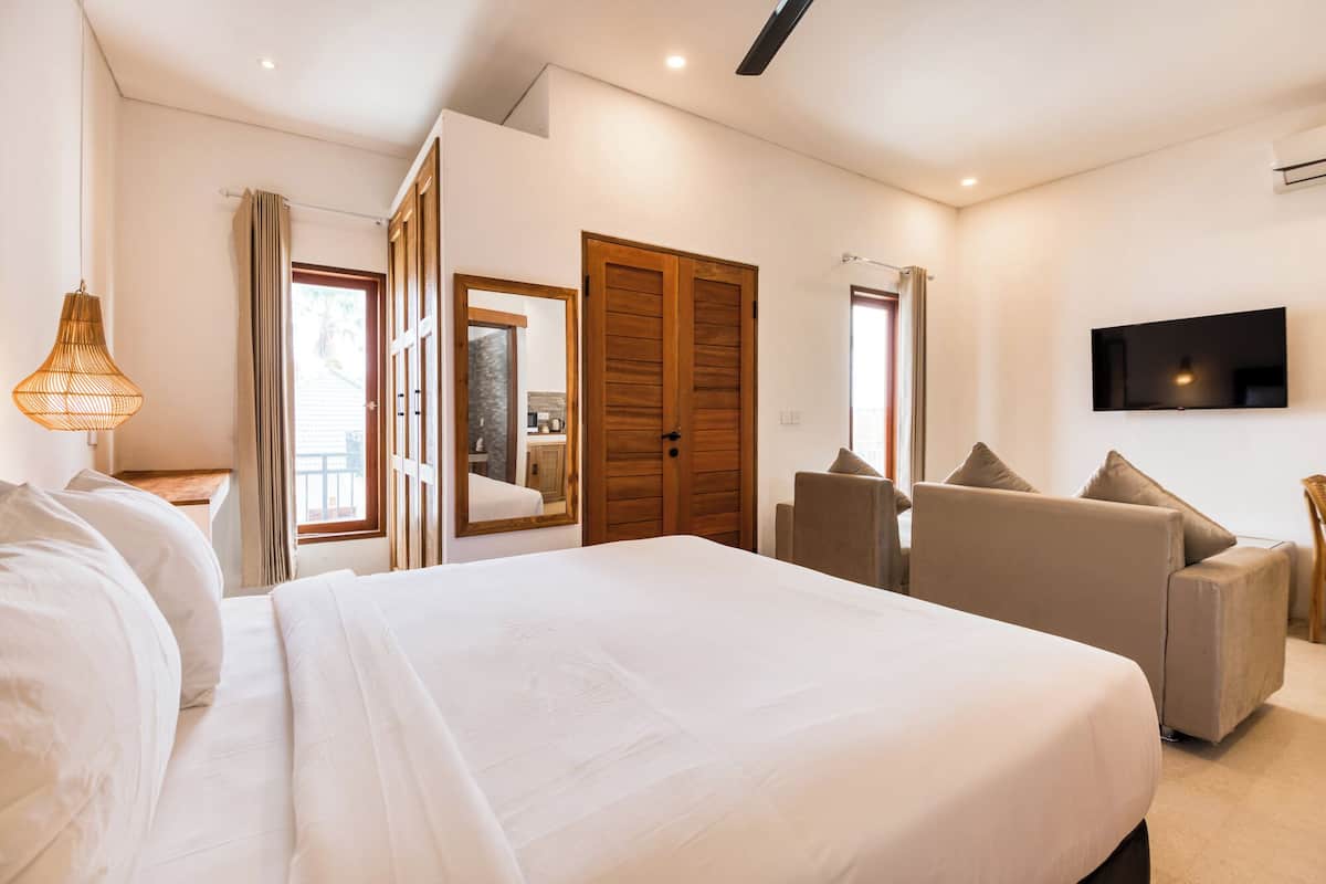 A bedroom with a large bed, a TV mounted on the wall, and a seating area with chairs.