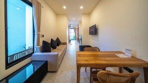 A hotel room with a sofa, a wooden table, a TV, and a window with curtains. - Lala Panzi Villa (Jimbaran)
