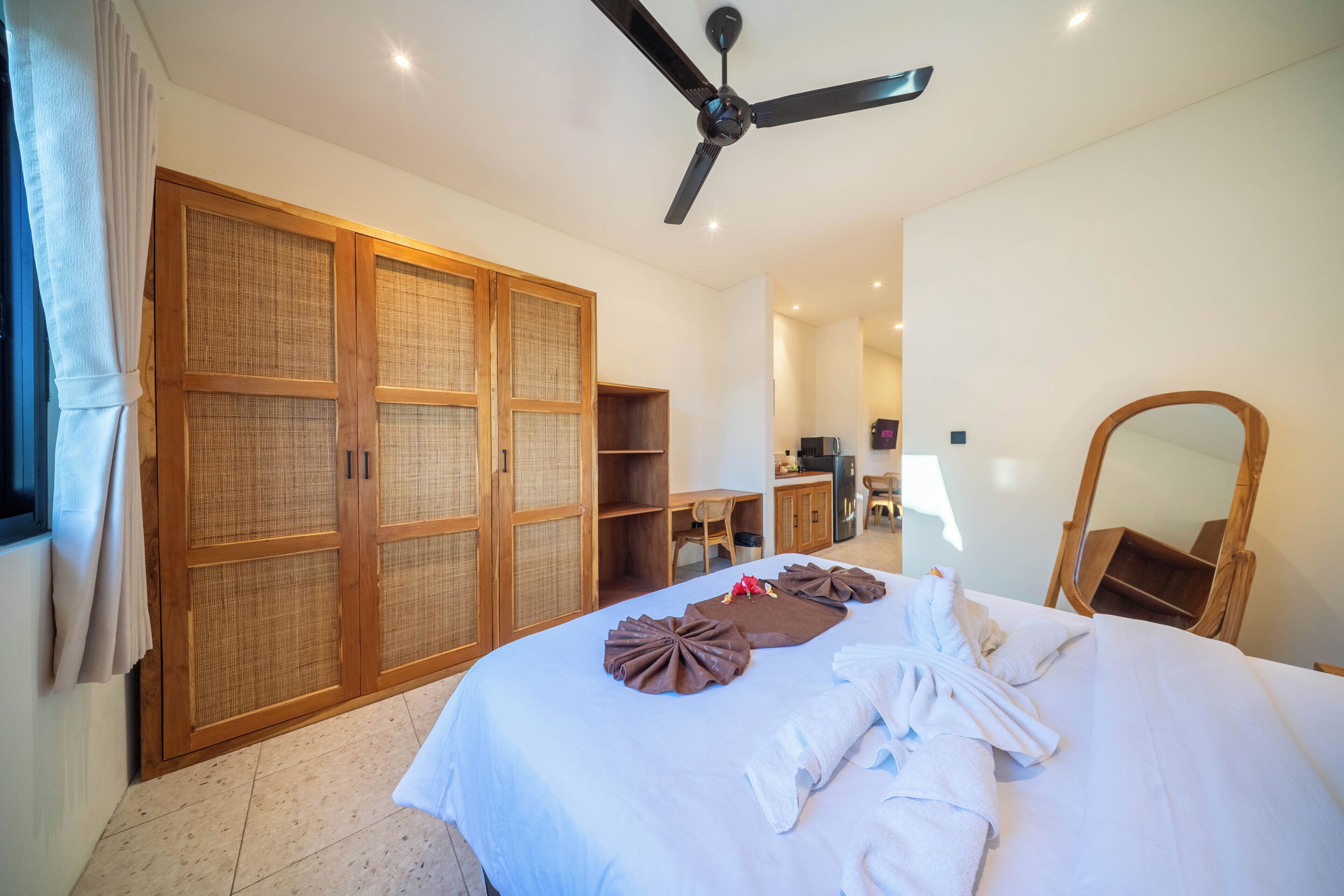 A hotel room with a bed, a ceiling fan, a wardrobe, a desk, and a mirror.
