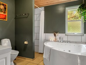 Een badkamer met een wit bad, toilet, douchegordijn, toiletrolhouder en een raam met begroeiing.