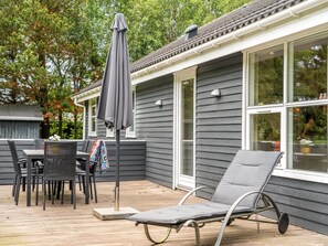 Une terrasse dotée de mobilier d’extérieur, notamment des chaises et un fauteuil de relaxation, ainsi qu’un grand parasol.
