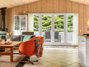 Una habitación acogedora con techo de madera, un sofá, una mesa con bebidas y un sillón con una manta colorida.