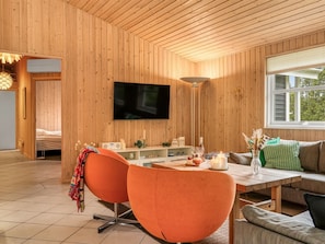 Una habitación con paneles de madera, un televisor, sillas anaranjadas, una mesa con velas y una ventana.