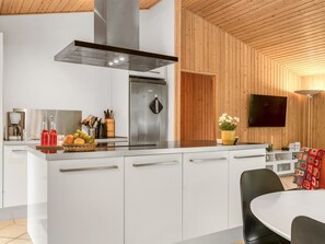 Une cuisine moderne dotée d’un îlot central, d’appareils électroménagers en acier inoxydable et d’un plafond en bois.