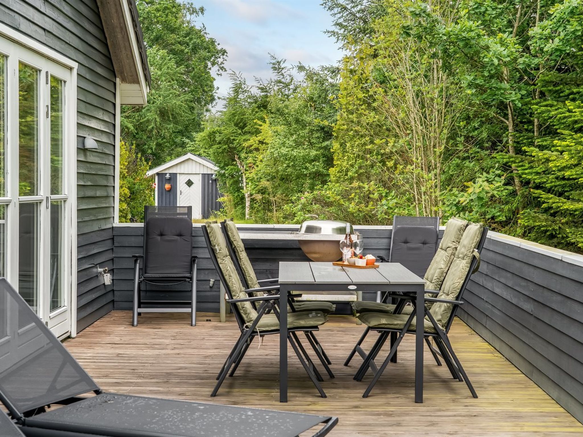 Une terrasse extérieure avec une table et des chaises, un barbecue et un abri de jardin en arrière-plan.