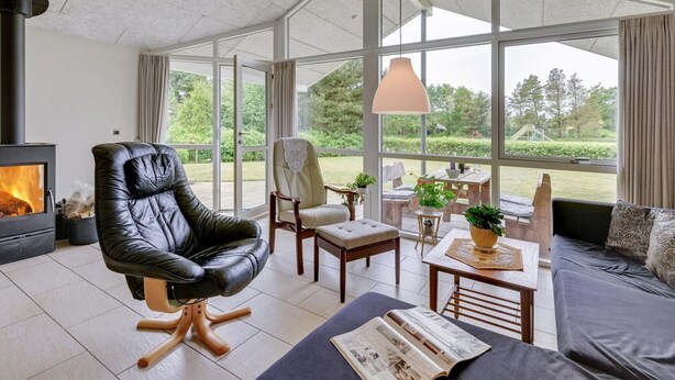Una sala de estar moderna con chimenea, un sillón de cuero, sofá y ventanas amplias que ofrecen vistas al exterior.