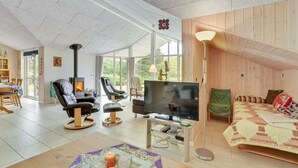 Amplia sala de estar con chimenea, asientos cómodos, televisor y un ventanal con vistas al exterior.