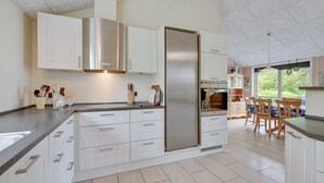 Una cocina moderna con armarios blancos, electrodomésticos de acero inoxidable y un comedor con sillas de madera.