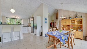 Una cocina amplia con electrodomésticos modernos, un comedor con mesa de madera y una sala de estar acogedora con muebles de madera y una estantería.