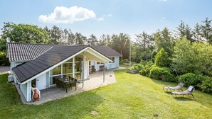 Una casa de dos plantas con un patio, un comedor y un jardín con sillones de descanso.