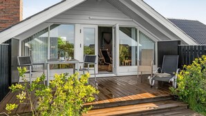 A modern house with a large glass door leading to an outdoor seating area with a table and chairs.