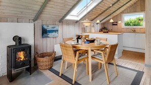 A cozy kitchen with a dining area, a wood-burning stove, and a large window overlooking greenery.