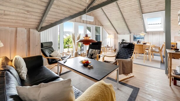 A spacious living area with a high ceiling, wooden walls, and large windows providing natural light.