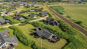 An aerial view of a residential area with houses, a railway track, and green fields.