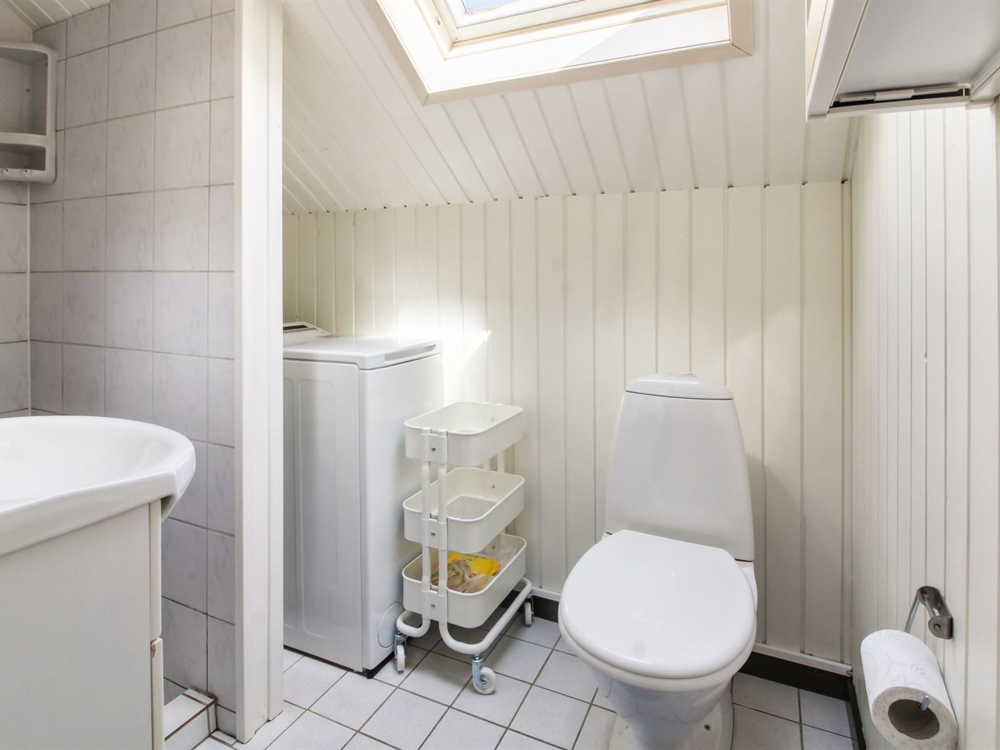 Een compacte badkamer met dakraam, toilet, een wasmachine en een klein wandrek.