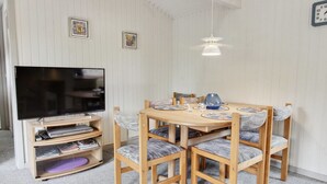 Ein Essbereich mit einem Holztisch und Stühlen, einem Fernseher auf einem Standfuß und einer Deckenleuchte.