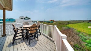 A wooden deck with a table and chairs, overlooking a grassy landscape and houses. - Beach Boardwalk, Pool Access & Ocean Views | Coral Reef by AvantStay (Port Aransas)
