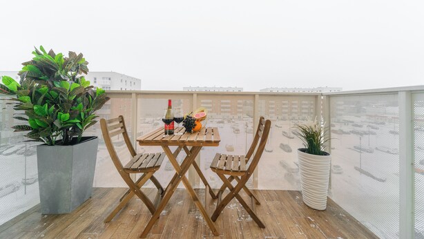 Une table en bois, des chaises et un pot de fleurs sont disposés sur un balcon d’où l’on peut admirer la vue sur les bâtiments.