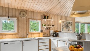 Een moderne keuken met houten wanden, witte kasten en een granieten aanrecht. Twee ramen zorgen voor natuurlijk licht, er hangt een klok aan de muur en er staan diverse keukenaccessoires en apparaten.