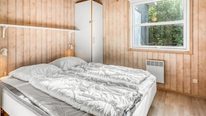 Een slaapkamer met houten wanden, een bed met wit beddengoed, een kledingkast, een raam met uitzicht op groen en een plafondventilator.