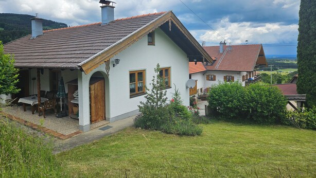 A traditional chalet with a sloped roof, wooden door, and a small porch with outdoor seating. - Ferienhaus für 5 Personen, 2 Seperate Schlafzimmer (Anger)