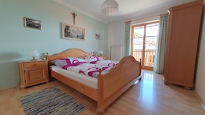 A bedroom with a wooden bed, a nightstand, a bedside table, a window with curtains, and a radiator. - Ferienhaus für 5 Personen, 2 Seperate Schlafzimmer (Anger)