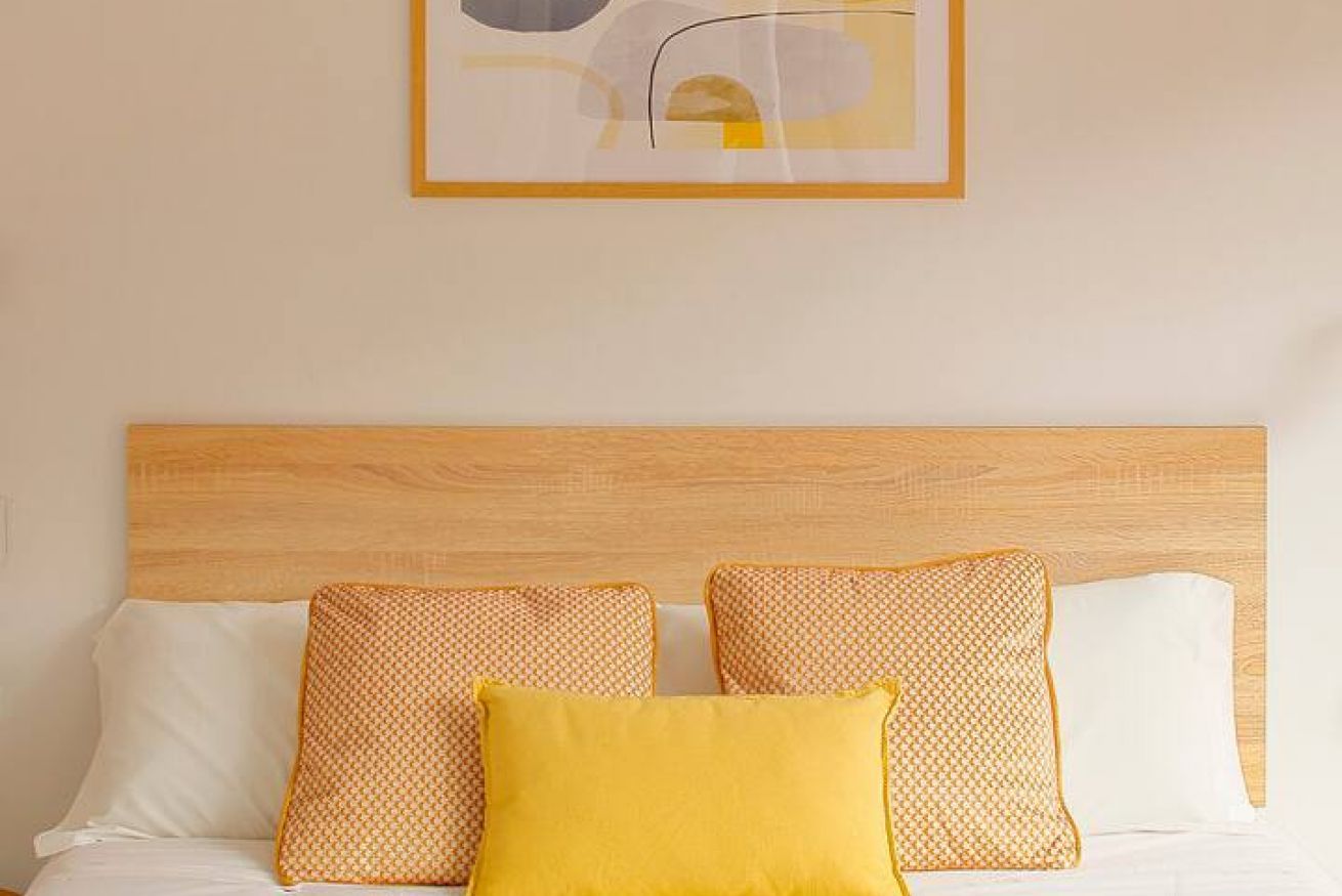 Un letto con una testiera in legno, tre cuscini e un quadro appeso alla parete.